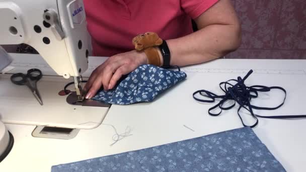 Uma mulher costura uma máscara de um tecido com uma impressão azul — Vídeo de Stock