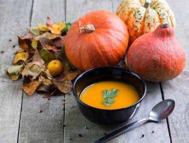 Doğal ahşap masa üzerinde siyah kase sonbahar balkabağı çorbası.