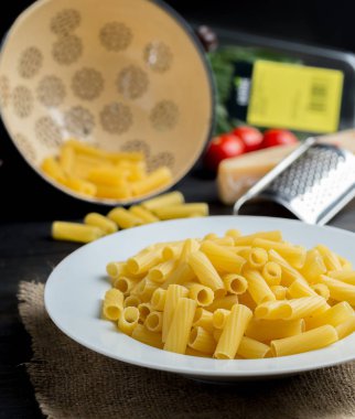 Doğal ahşap masa üzerinde beyaz tabak içinde pişmemiş makarna.