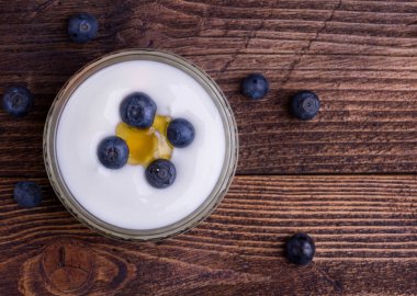 Ahşap rustik masa üzerinde tüm yaban mersini ile cam kapta beyaz yoğurt. Detay.