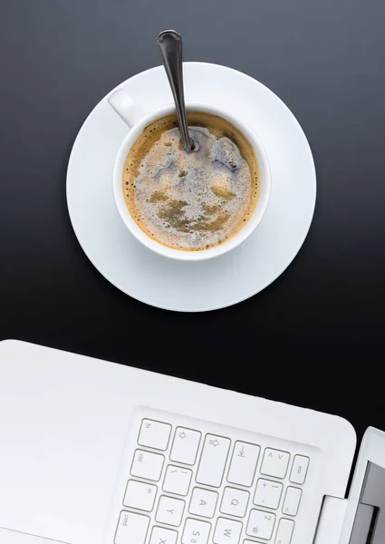 Biały filiżankę kawy na ciemnym tle z laptopa. Widok z góry. — Zdjęcie stockowe