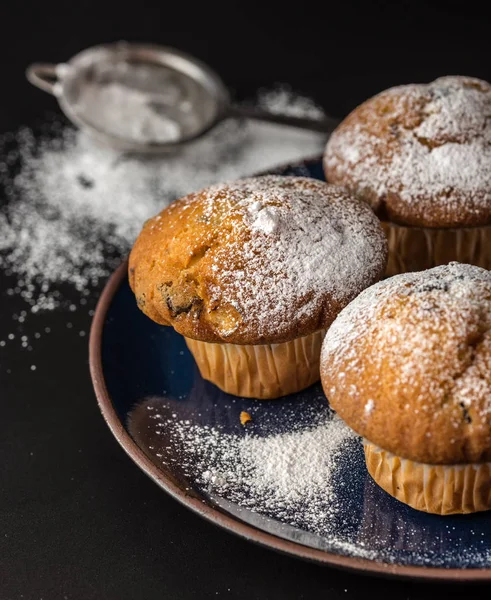 Muffins mit Puderzucker bestreut auf blauem Teller mit Sieb dahinter. — Stockfoto