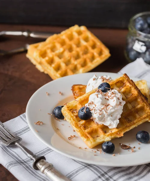Belgian waffles on white plate, napkin and rustic background.