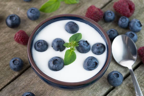 Tigela de mirtilos inteiros em iogurte branco na mesa de madeira rústica — Fotografia de Stock
