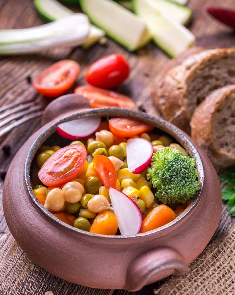 Salade de légumes dans un bol artisanal avec du pain sur une table en bois . — Photo
