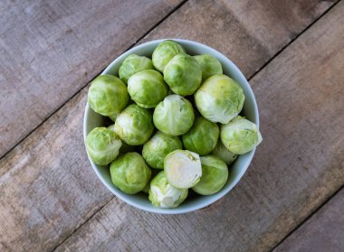 Ahşap masa üzerinde beyaz kase çiğ Brüksel lahanası. Üstten Görünüm.