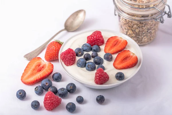 Yoghurt i vit skål med jordgubbar och blåbär på vit bakgrund. — Stockfoto