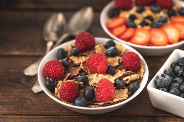 Böğürtlenli granola cipsi ve ahududu, siyah ahşap masada beyaz kasede..