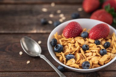 Böğürtlenli granola cipsi ve ahududu, siyah ahşap masada beyaz kasede..