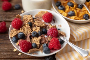 Böğürtlenli mısır gevreği ve ahududu, beyaz kasede, siyah ahşap masada..