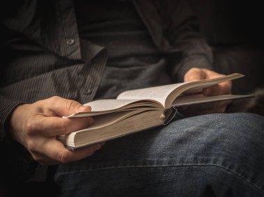 Kanepede siyah gömlekli kitap okuyor..