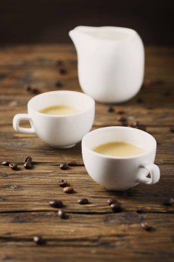 İki bardak sıcak güçlü kahve, süt ve kahve çekirdekleri ahşap tablo vazo
