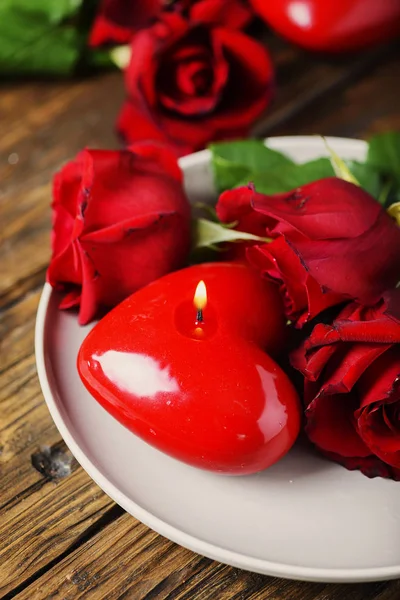 Red heart candles and roses on wooden table