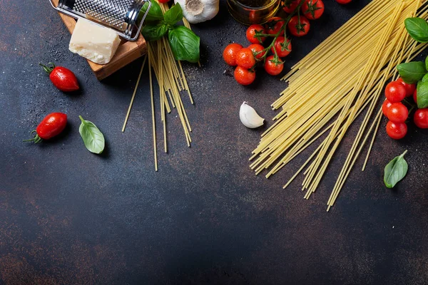 İtalyan yemeği kavramı: spagetti, domates, fesleğen, sarımsak, peynir ve siyah masadaki zeytinyağı. Kopyalama alanı olan üst görünüm
