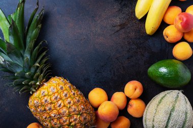 Sağlıklı vejetaryen yemeği kavramı. Ananas, muz, kayısı, kavun, siyah arka planda avokado. En üst görüntü