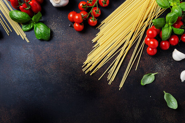 Ingredients for cooking italian pasta: spaghetti, tomato, basil and garlic on the black table. Top view image with a copy space