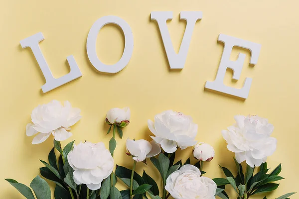 黄色背景上的白色典雅牡丹 上面有木制的字母 贺卡的概念 爱情的概念 顶视图 — 图库照片