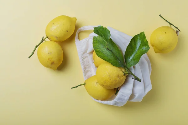 生物学的健康食品とゼロ廃棄物の概念 黄色の背景に綿のショッピングバッグに緑の葉を持つ新鮮な生物学的レモン コピースペース付きのトップビュー画像 — ストック写真