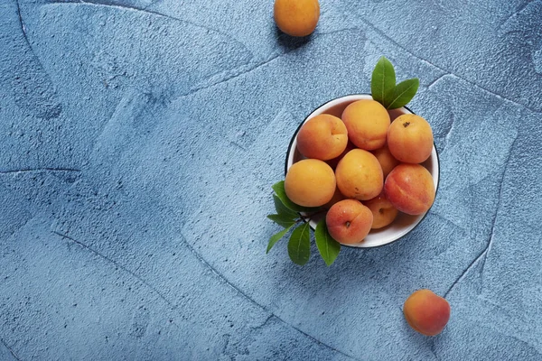 Sweet fresh apricots in the white bowl on the blue back ground. Top view image with copy space