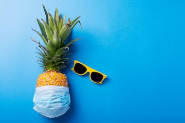 2020 yaz tatili kavramı. Tıbbi maskeli çam elması ve mavi arka planda güneş gözlüğü. En üst görüntü