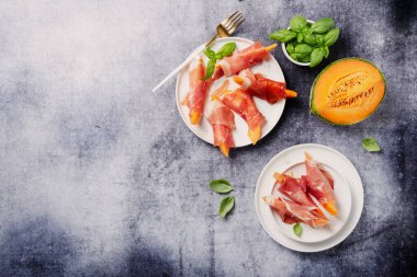 Tatlı kavun ve koyu arkaplanlı jambonlu yaz aperatifi. Kopyalama alanı olan en üst görüntü