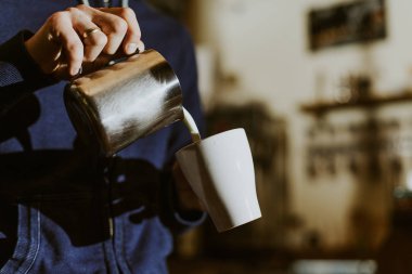 Kahve makinesiyle sütü buharda pişiren barista kafede latte sanatı yapmaya hazırlanıyor.