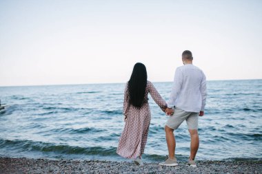 Sahilde el ele tutuşan bir çiftin arka görüntüsü..