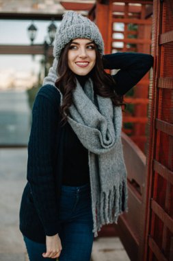 Güzel neşeli kız mavi örgü şapka ve atkıyla poz veriyor, gri renkte izole edilmiş.