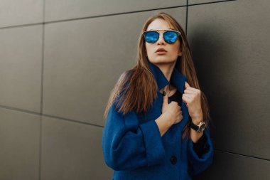 Gri arka planda duran mavi ceketli genç kız.