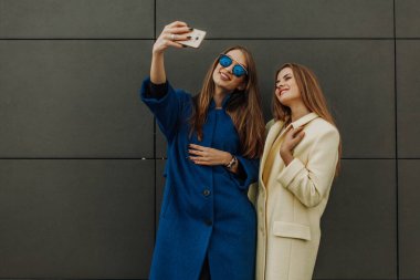 Paltolu iki güzel kız birlikte yürüyüp, selfie çekiyorlar.