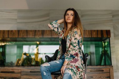 Şık esmer kadın arka plandaki akvaryumda oturuyor.