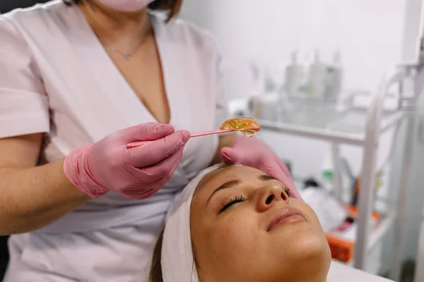 Close up of beautician (cosmetologist) applying chemical peel treatment on patient in a beauty spa, for skin rejuvenation, complexion and acne beauty treatments.