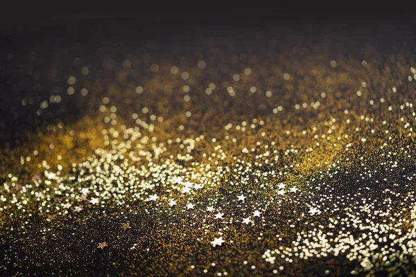 Beautiful Christmas light background. Abstract glitter bokeh and scattered sparkles in gold color, on black — Stock Photo, Image