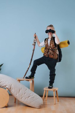 Evde yürüyüş yapan küçük çocuk. Dürbünle bakıyor, asayı tutuyor.