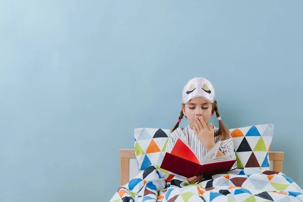 Gaap klein meisje is het lezen in bed in pyjama voor het slapen gaan over blauw — Stockfoto