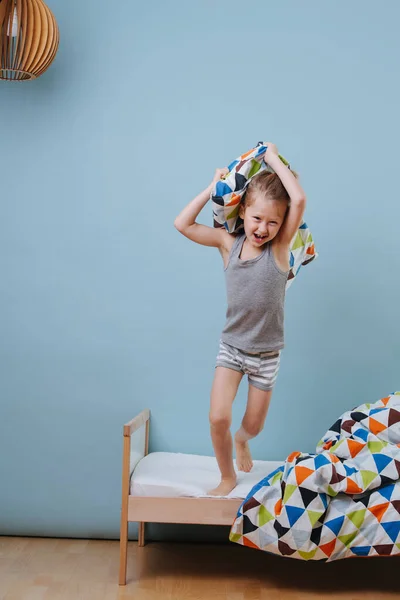 Little boy jumping from bed, armed with a pillow over blue walls — Stock Photo, Image