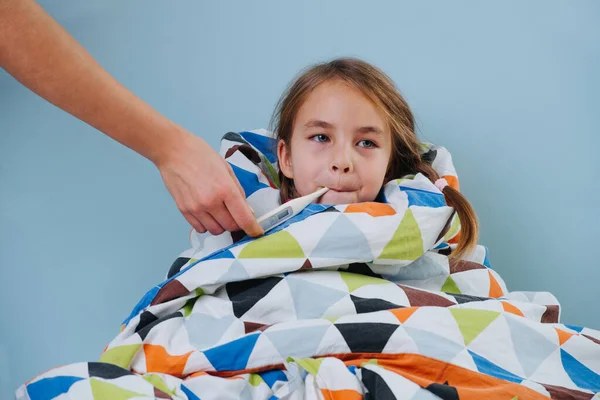 Niña enferma con resfriado común sentada en la cama debajo de una manta con termómetro — Foto de Stock