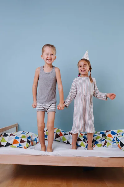 Boy and girl holding hands, jumping on the bed together — Stock Photo, Image