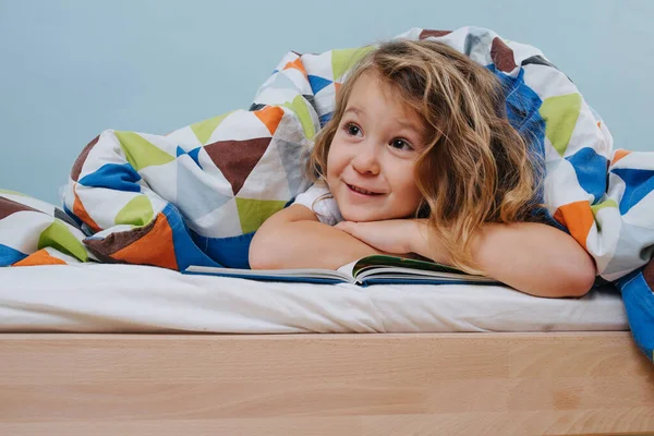 Adorable little girl reading in bed under blanket looking at parents — Stock Photo, Image