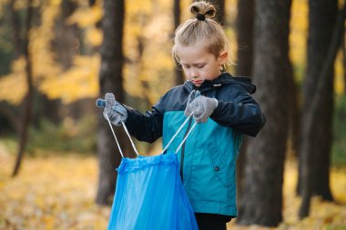 Küçük çocuk sonbaharda mevsimlik bir ormanda çöp torbası topladı.