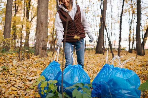 Kvinna som tar blå plastpåse till en hög i en säsongsbetonad skog på hösten. — Stockfoto