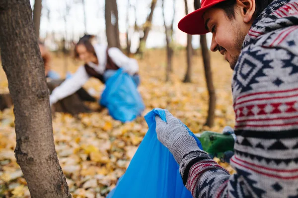 Mevsimlik bir ormanda sonbaharda çöpleri toplayan çömelmiş bir adamın yakınına. — Stok fotoğraf