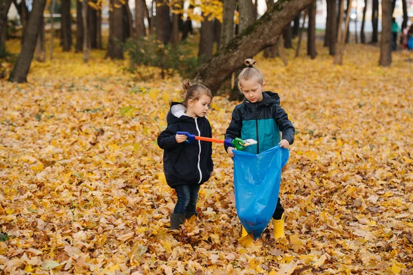 Μικρά αδέλφια συλλέγουν σκουπίδια χρησιμοποιώντας συλλέκτη απορριμμάτων σε ένα δάσος το φθινόπωρο — Φωτογραφία Αρχείου