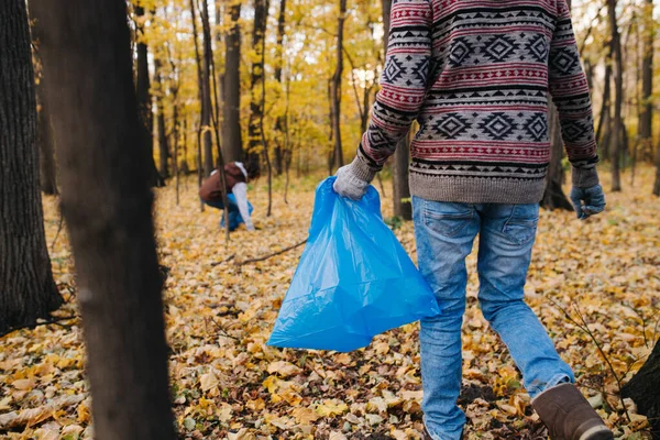 El primer plano de la parte inferior del hombre con la bolsa de basura en el bosque estacional en otoño . — Foto de Stock