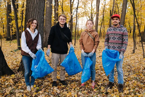 Retrato grupal de voluntarios con bolsas de basura en un bosque estacional en otoño — Foto de Stock