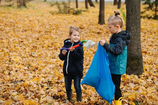 Hermanos pequeños recogen basura usando recolector de basura en un bosque en otoño — Foto de Stock