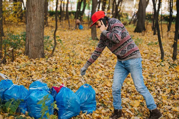Un hombre junto a una pila de basura en un bosque arreglando la eliminación de basura por teléfono . — Foto de Stock