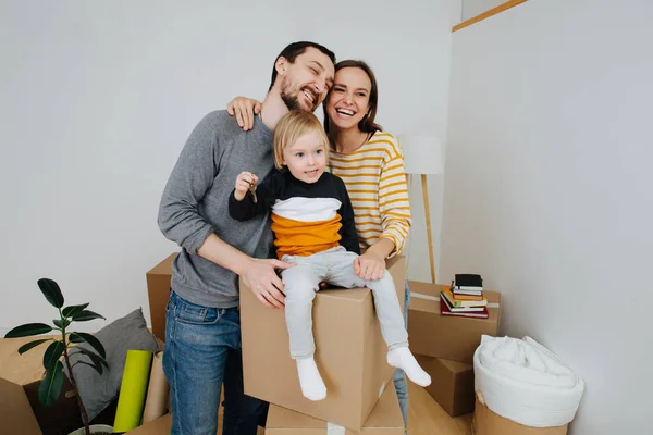 Jovem família feliz se mudando para uma nova casa, criança segurando chaves — Fotografia de Stock