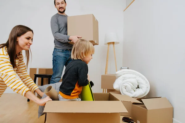 Happy young family moving to a new home, unpacking cardboard boxes with joy