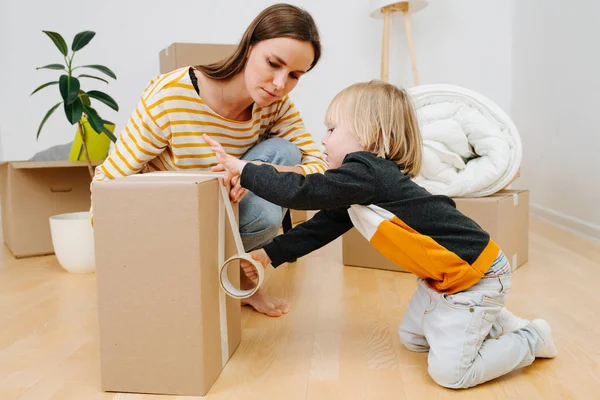 Son helping mother to pack, sealing box with scotch tape. they are moving out. — Stock Photo, Image